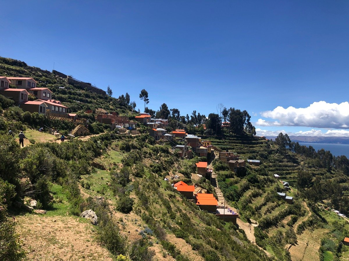 Houses with orange roofs and terraced fields on the steep hillside of Yumani Village, Isla del Sol, with Lake Titicaca in the background.