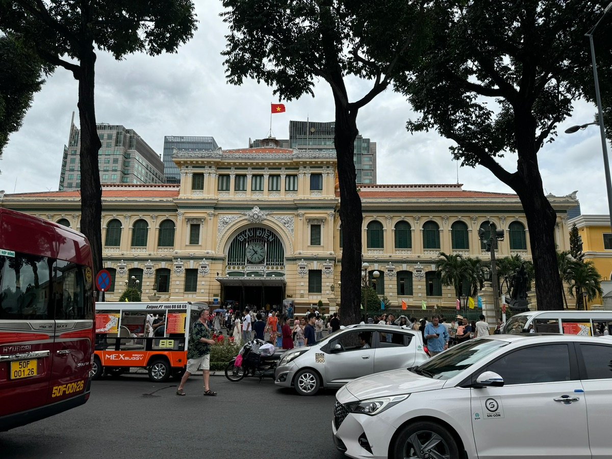 A broader view of the statue and the scaffolding-covered cathedral, with people in the foreground and a glimpse of other buildings.