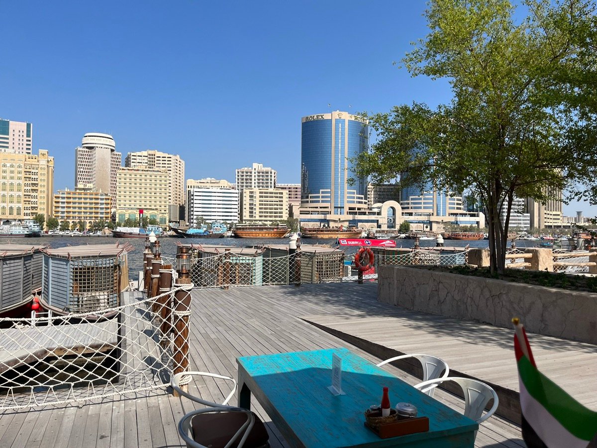 A vibrant waterside view of Dubai Creek from Al Seef, featuring traditional boats and a modern skyline in the distance