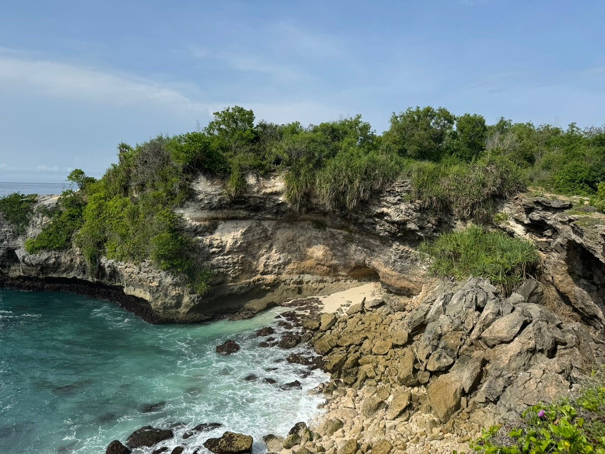 Overview of Tegal Wangi Beach from the cliff, showing rocky shore and turquoise waves