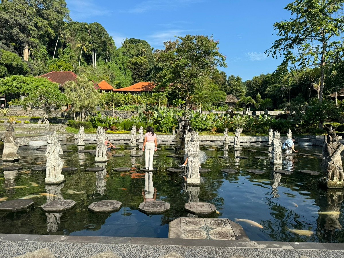 Path leading through Tirta Gangga water garden with stone statues and lush trees
