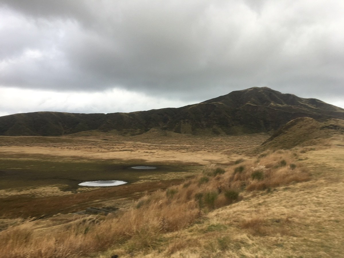 Child walking on dry grassy plains of Aso caldera towards mountains