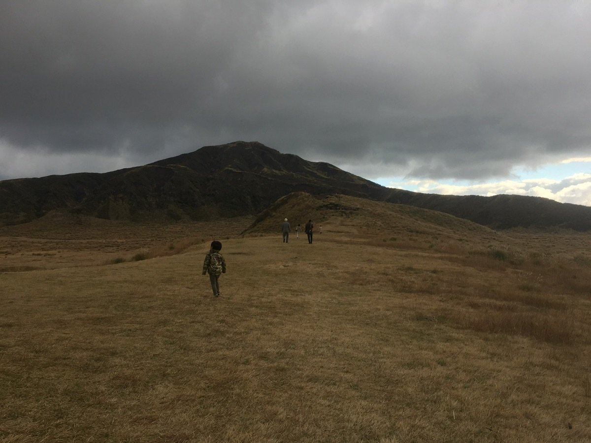 Hikers on Kusasenri-ga-hama plain with Mount Aso peaks in background