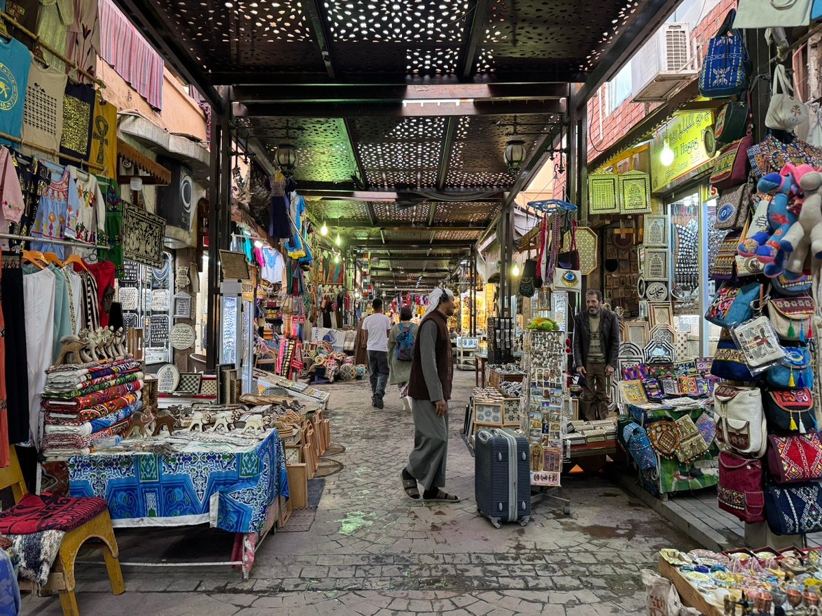 开罗汗哈利利集市一条熙熙攘攘的小巷，头顶是华丽的穿孔天花板，两旁摆满了色彩斑斓的商品