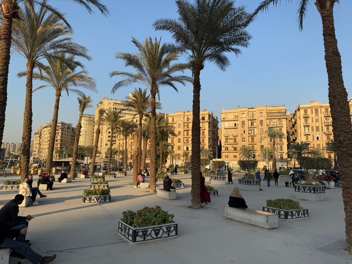 Close-up of a person walking on the sidewalk in Mansheya Square, carrying a white bag.