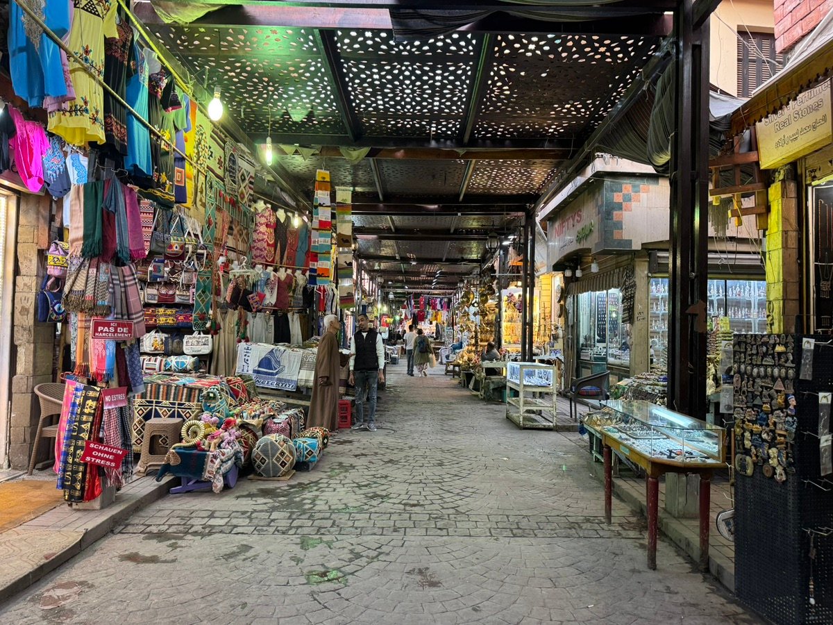 人们在开罗汗哈利利集市中行走，展示着纪念品摊位和鹅卵石小径