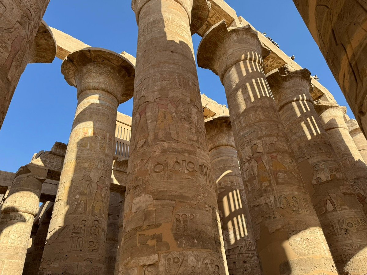 Partially ruined pylon at Karnak Temple with rubble and palm trees.