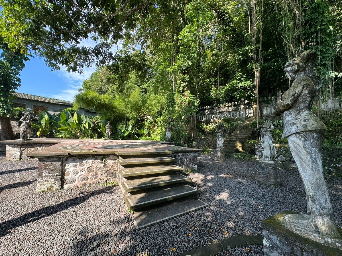 People walking on stepping stones among ornate stone statues in the water at Tirta Gangga