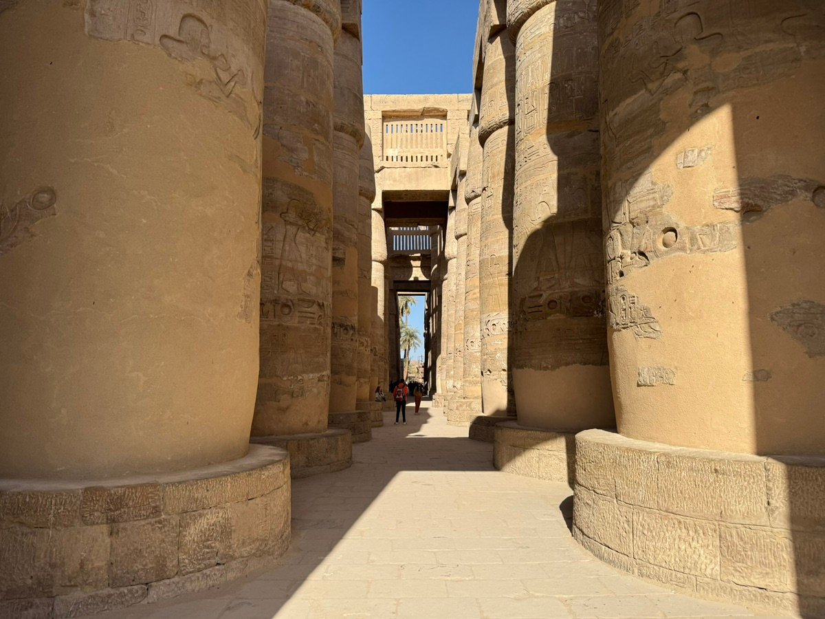Massive stone walls of Karnak with palm trees against a blue sky.