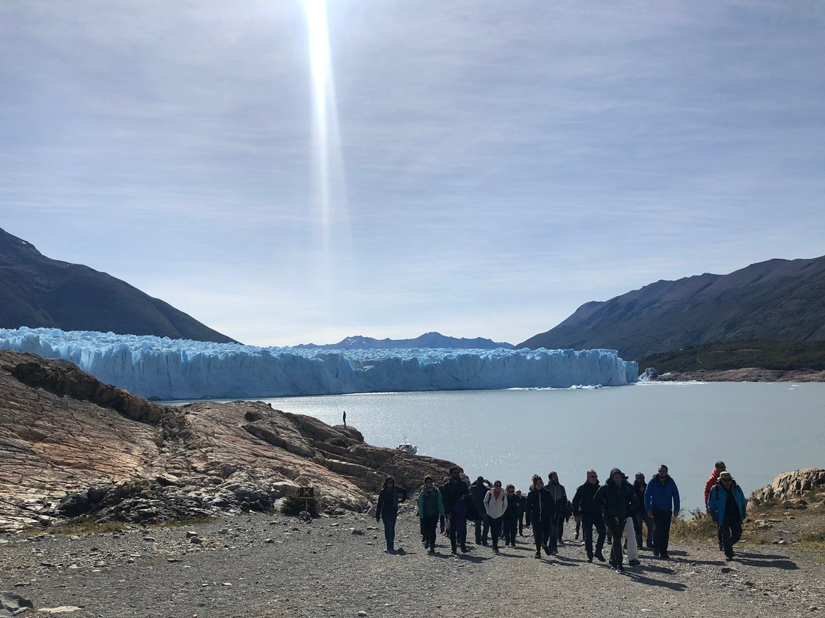 People standing on the rocky shore looking at the glacier