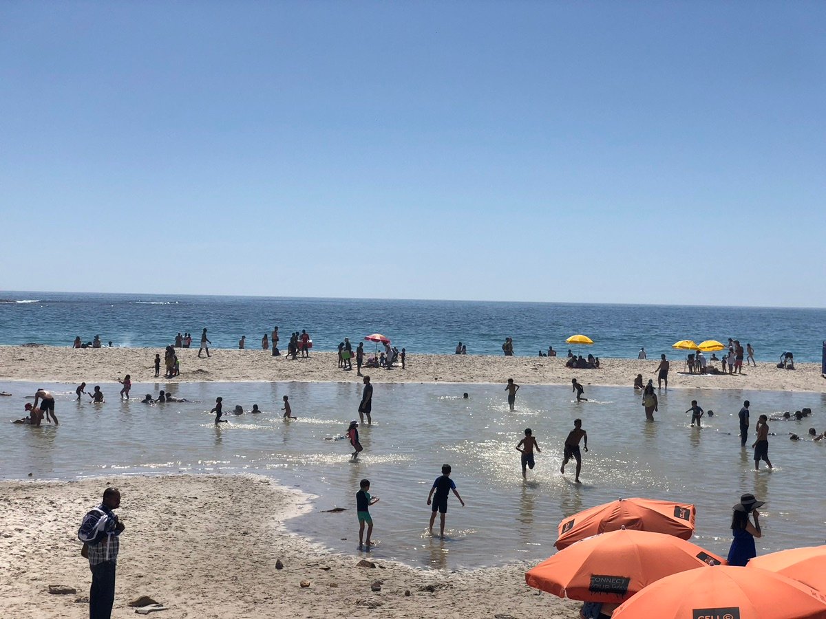 Crowded Camps Bay promenade with people walking and cars parked