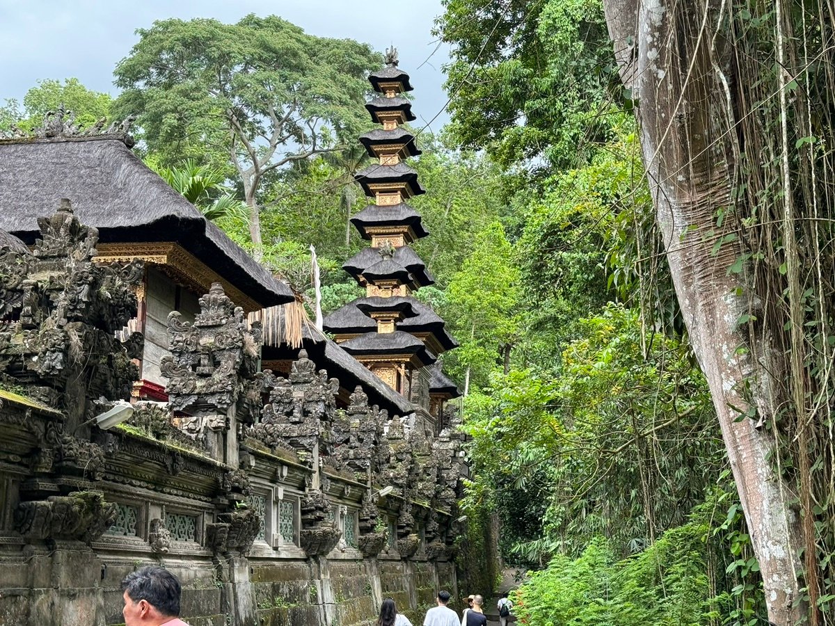 Main temple building with a dark tiled roof and a smaller thatched shrine at Gunung Kawi
