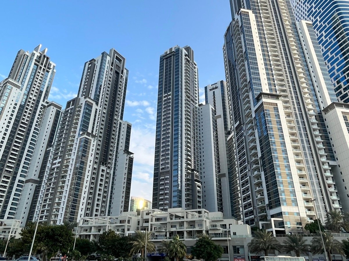 The distinctive wavy blue skyscraper of Sky Gardens (Park Towers) next to a white multi-story building in Dubai.