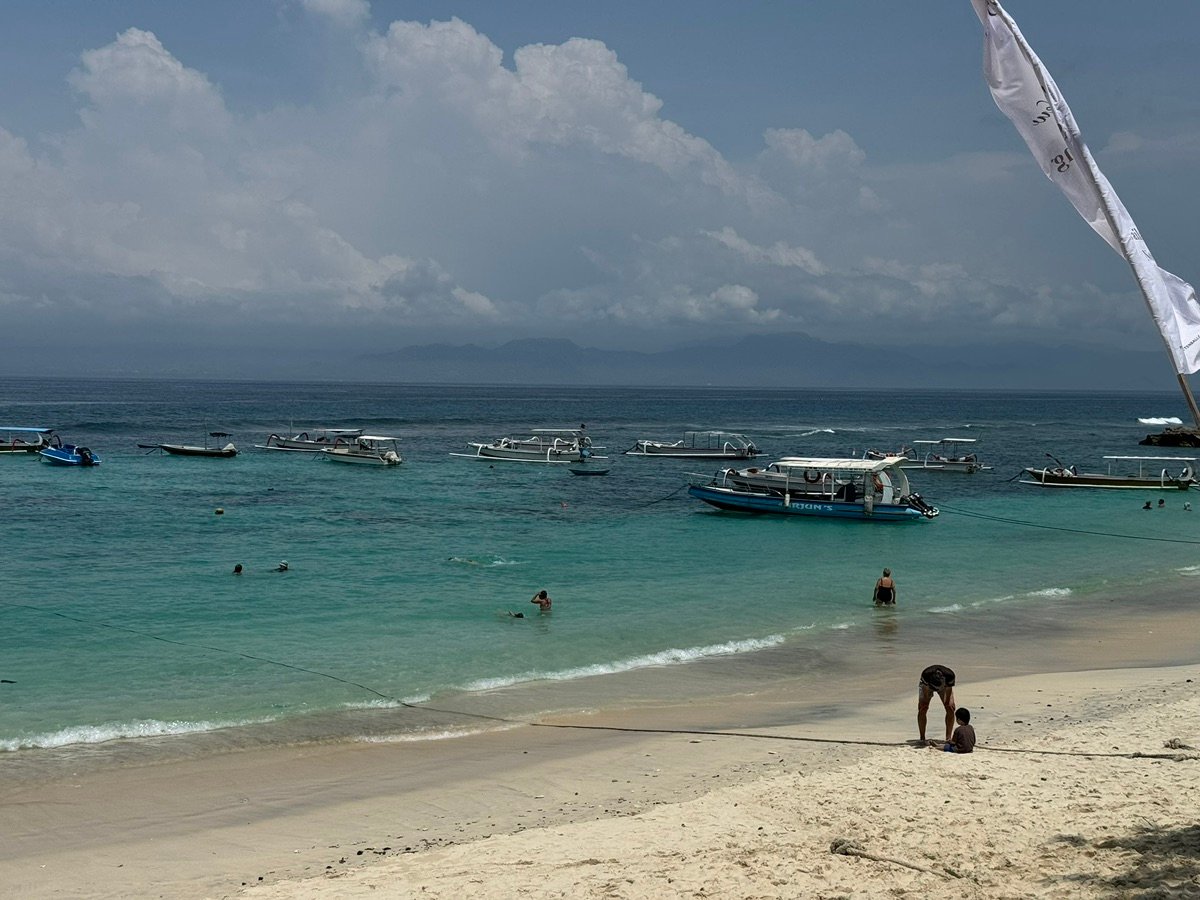 Gente nadando en las aguas turquesas de Mushroom Bay con barcos cerca de la orilla
