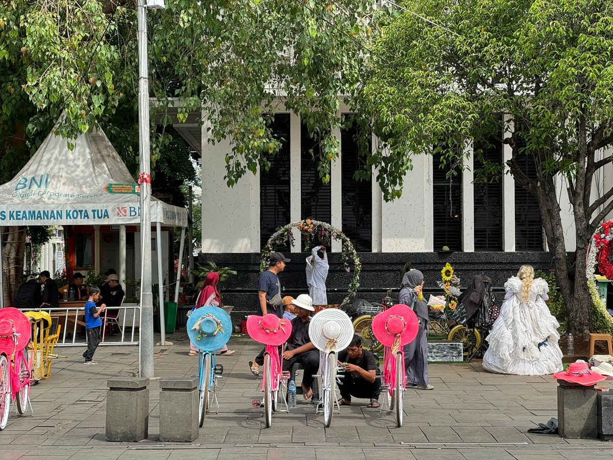 Woman in a hat next to a blue bicycle, with people milling around the square