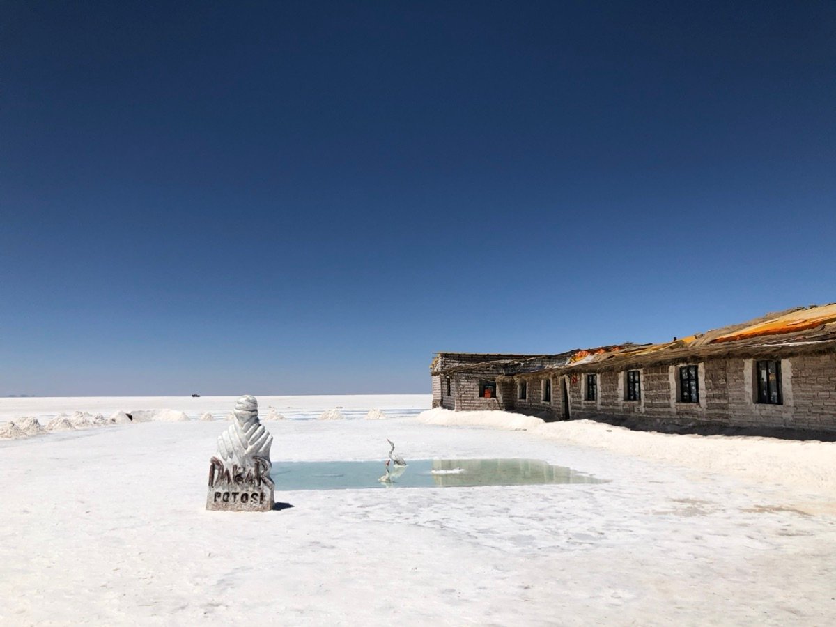 A salt building and the Dakar monument on the vast white expanse of Salar de Uyuni.