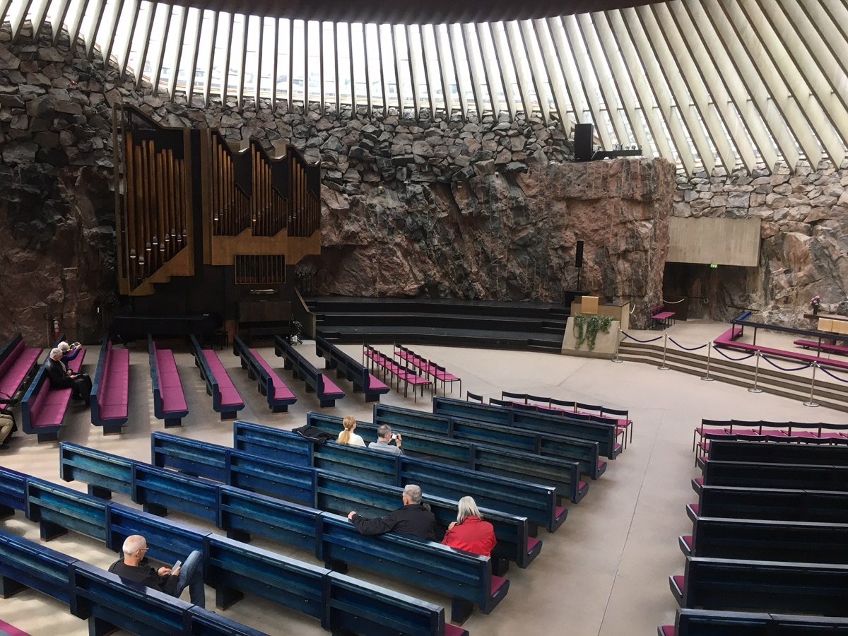The interior of Helsinki's Temppeliaukio Church, featuring rock walls and colorful pews.