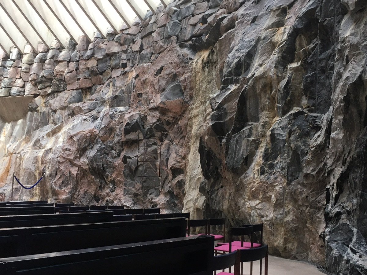Rugged rock walls and wooden pews inside Temppeliaukio Church in Helsinki.
